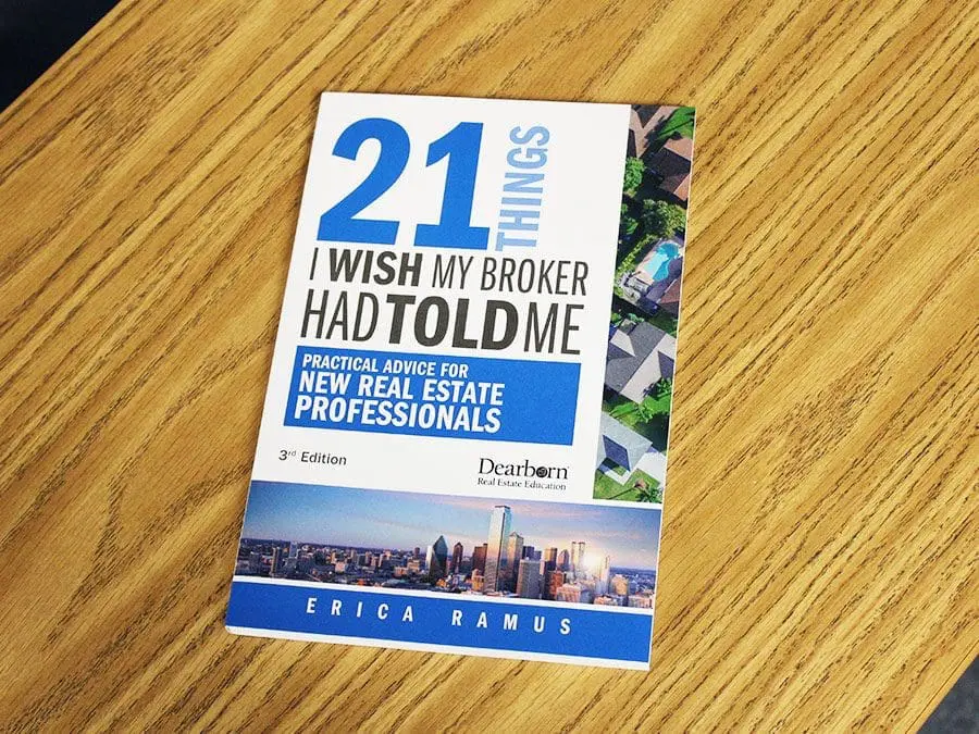 Cover of the book titled "21 Things I Wish My Broker Had Told Me: Practical Advice for New Real Estate Professionals" by Erica Ramus. The book is the 3rd edition and published by Dearborn Real Estate Education. The cover features a blue and white design with a city skyline at the bottom and an aerial view of houses on the right. The book is placed on a wooden surface.