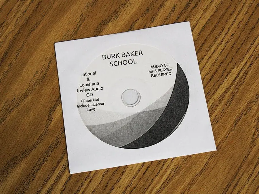 Image of a CD titled "BURK BAKER SCHOOL" in a paper sleeve on a wooden surface. The CD includes text mentioning "National & Louisiana Review Audio CD" and states "Does Not Include License Law." It also notes "AUDIO CD MP3 PLAYER REQUIRED."